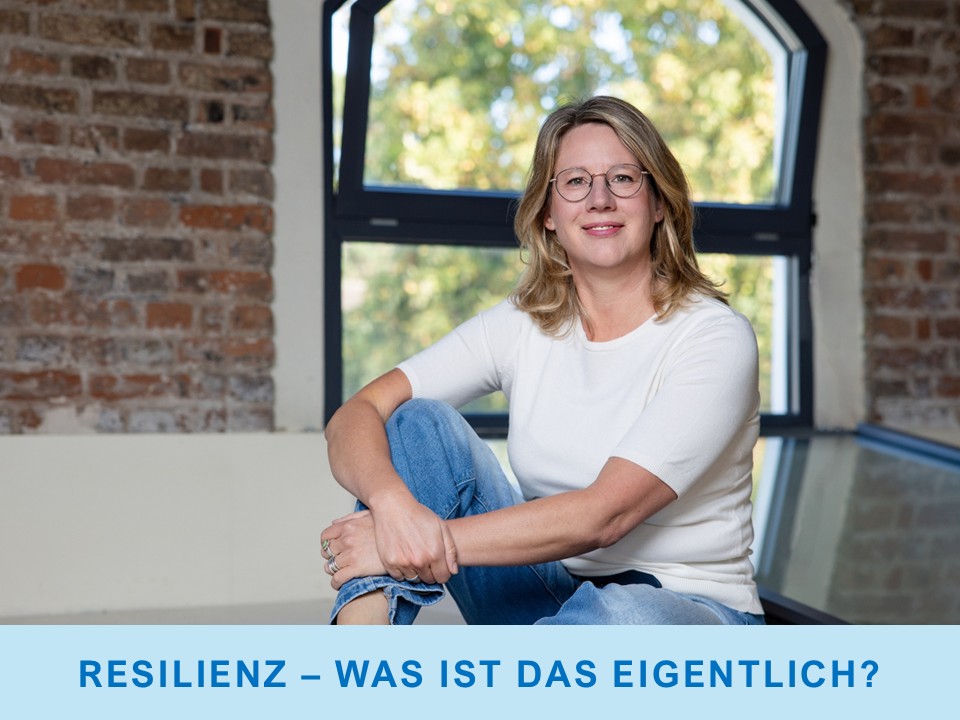 Stefanie Kappus sitzt mit angewinkeltem Knie auf einem Podest vor einer Ziegelstein-Wand
