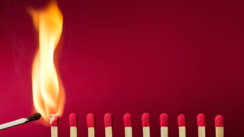 Eine Reihe frischer Streichhölzer mit rotem Kopf nebeneinander. Das erste Streichholz wurde mit einem brennenden Streichholz angezündet und eine helle Flamme züngelt auf.