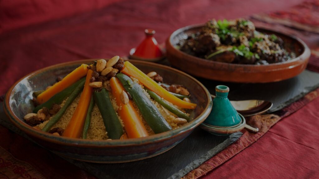 Zwei orientalische Tonschalen gefüllt mit Reis, Gemüse und Fleischbällchen, angerichtet auf einer dunkelrot-glänzenden Tischdecke.